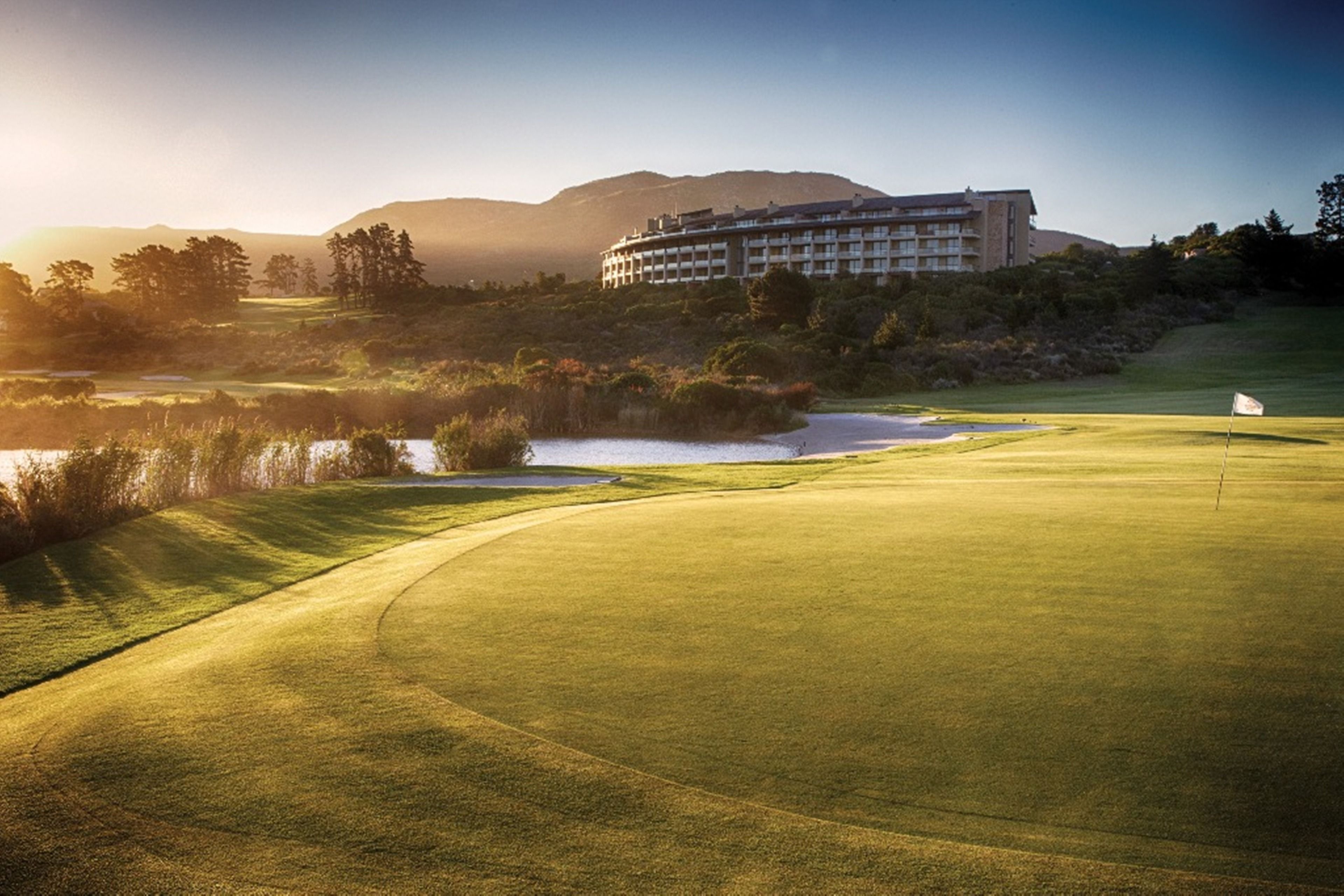 A golf course with a large building in the background, surrounded by trees and hills.