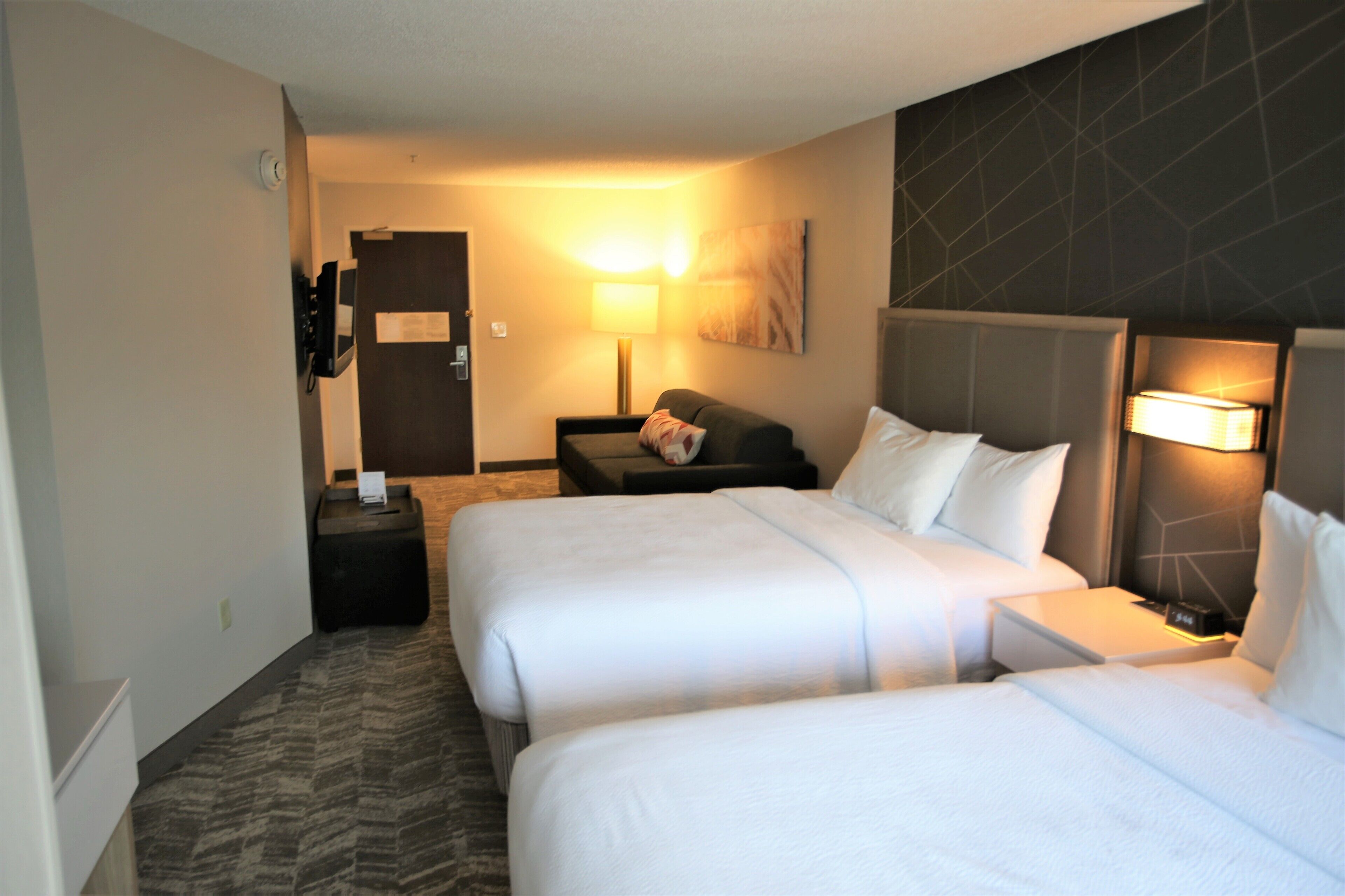 A hotel room with two beds, a sofa, a TV, and a lamp.