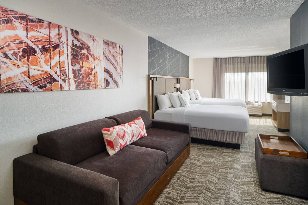 Una habitación de hotel con sofá, cama, televisor y un cuadro abstracto grande en la pared.