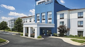 A modern hotel with a blue and white facade, a covered entrance, and a parking lot.