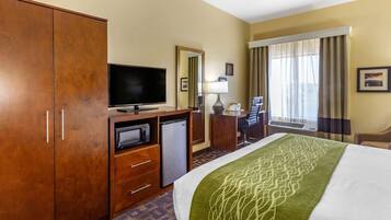 Een hotelkamer met een groot bed, een televisie, een bureau met stoel, een kledingkast en een kleine koelkast.