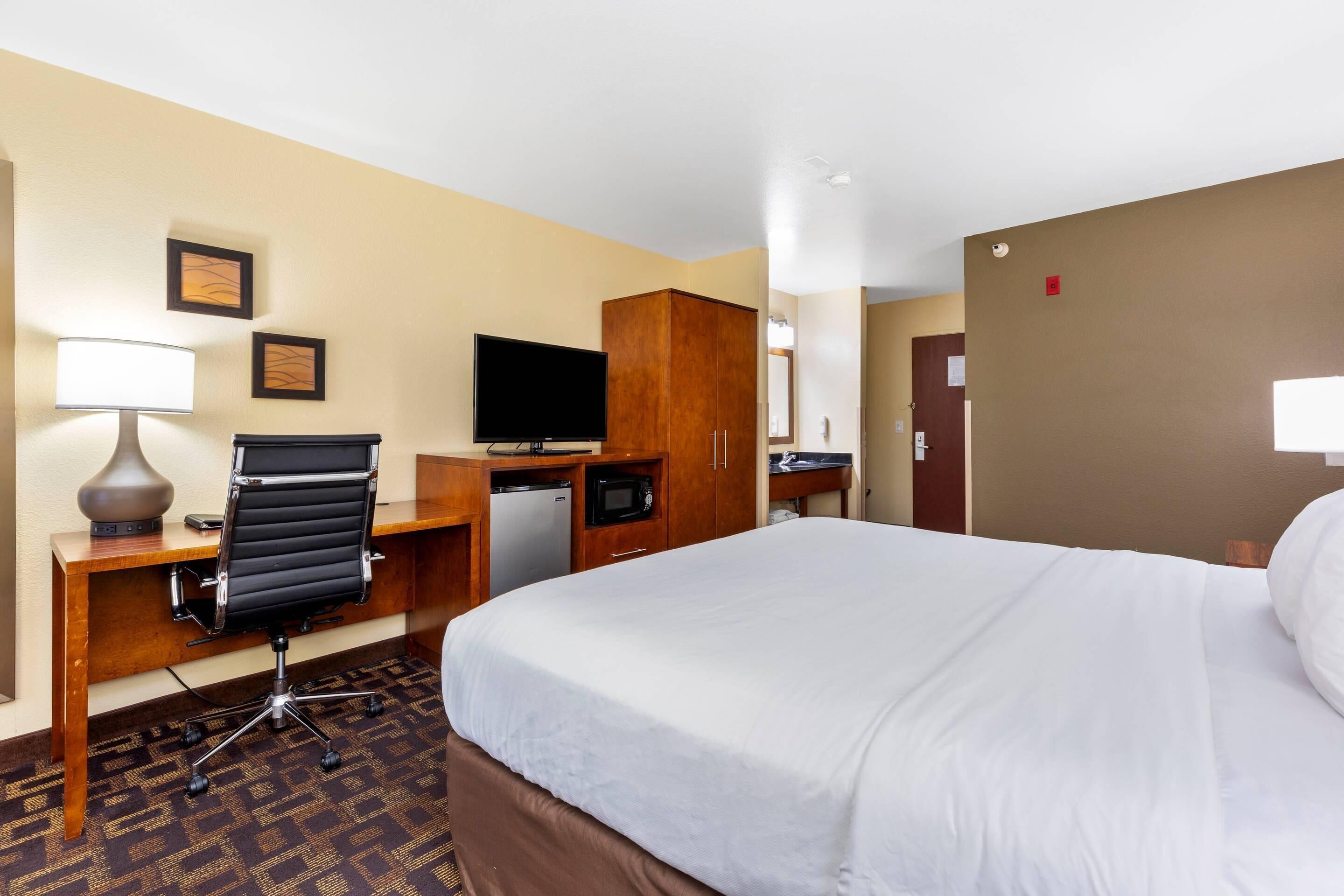 Habitación de hotel con una cama grande, un escritorio con computadora, televisión y un refrigerador pequeño.