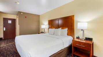 Habitación de hotel con una cama grande, dos mesitas de noche con lámparas, un cabecero de madera y piso alfombrado.