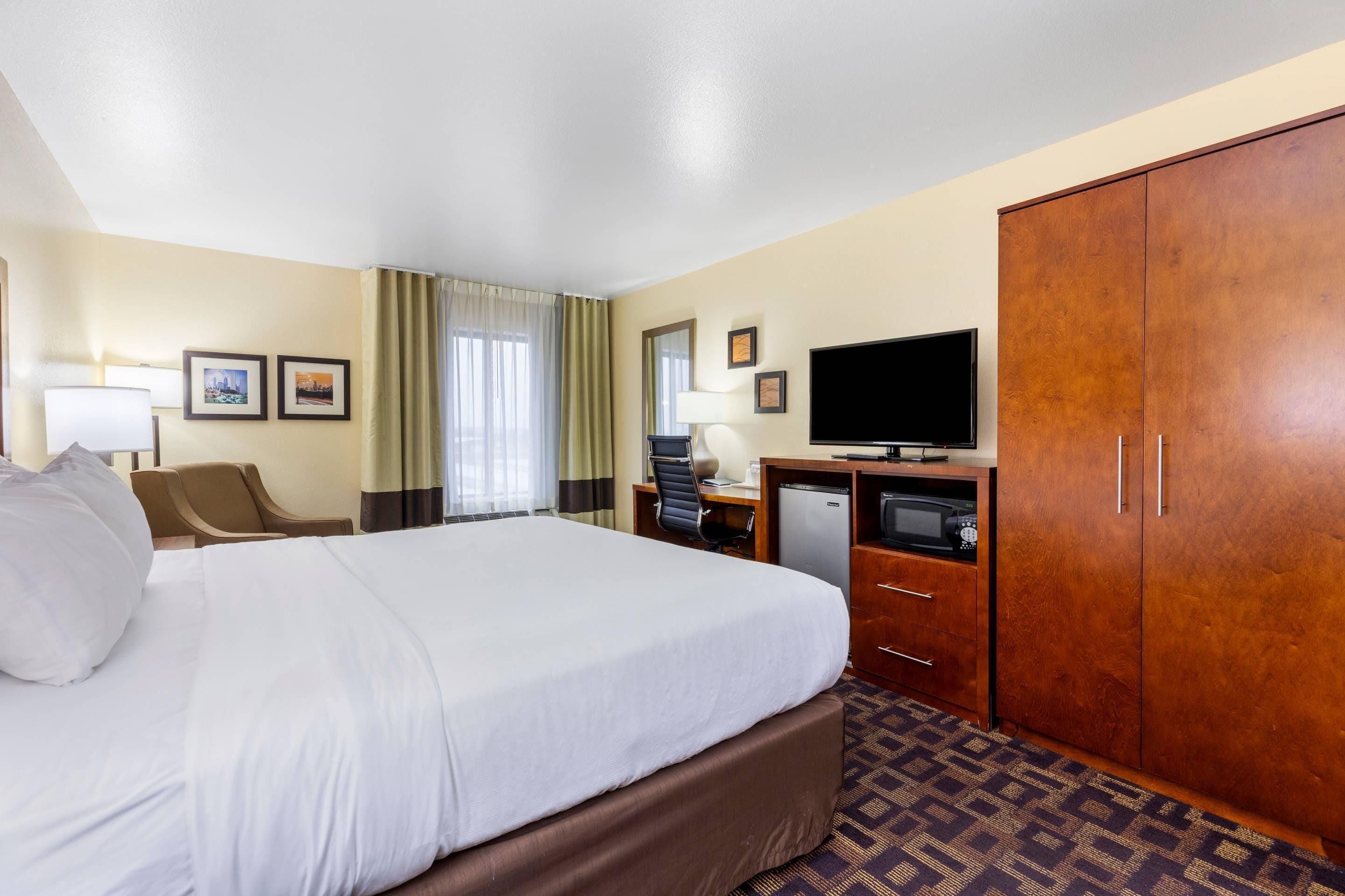 Ein Hotelzimmer mit einem großen Bett, einem Schreibtisch mit Computer, einem Fernseher und einem Kleiderschrank.