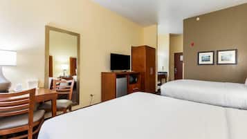Habitación de hotel con dos camas, un escritorio con silla, televisor, minibar y espejo.
