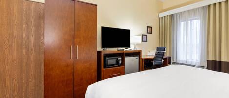A hotel room with a large bed, a wardrobe, a desk with a television, a microwave, and a refrigerator.