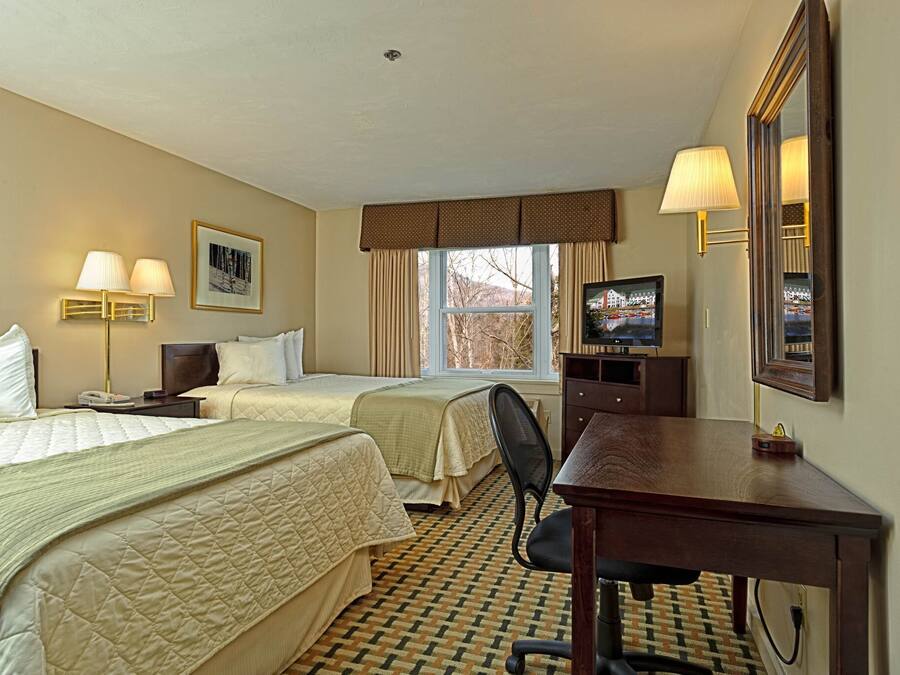 A hotel room with two beds, a desk, a chair, a television, and a window with curtains.