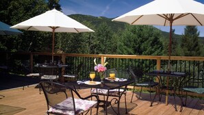 An outdoor deck with tables and chairs, white umbrellas, and a scenic mountain backdrop.