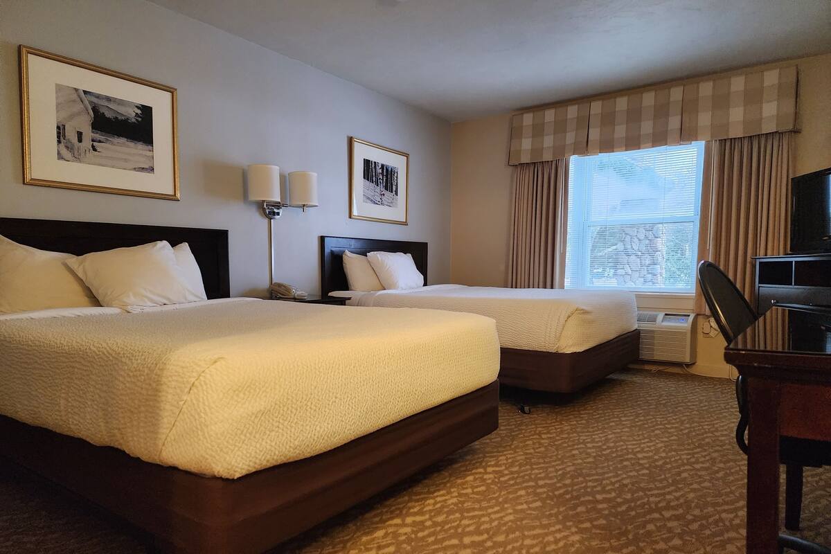 A hotel room with two beds, a desk, a chair, a TV, and two framed pictures on the wall.