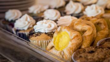 A variety of baked goods including muffins and pastries, some with whipped cream on top.