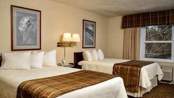 Une chambre d’hôtel avec deux lits, une grande fenêtre avec des rideaux, une lampe fixée au mur et des œuvres d’art encadrées.