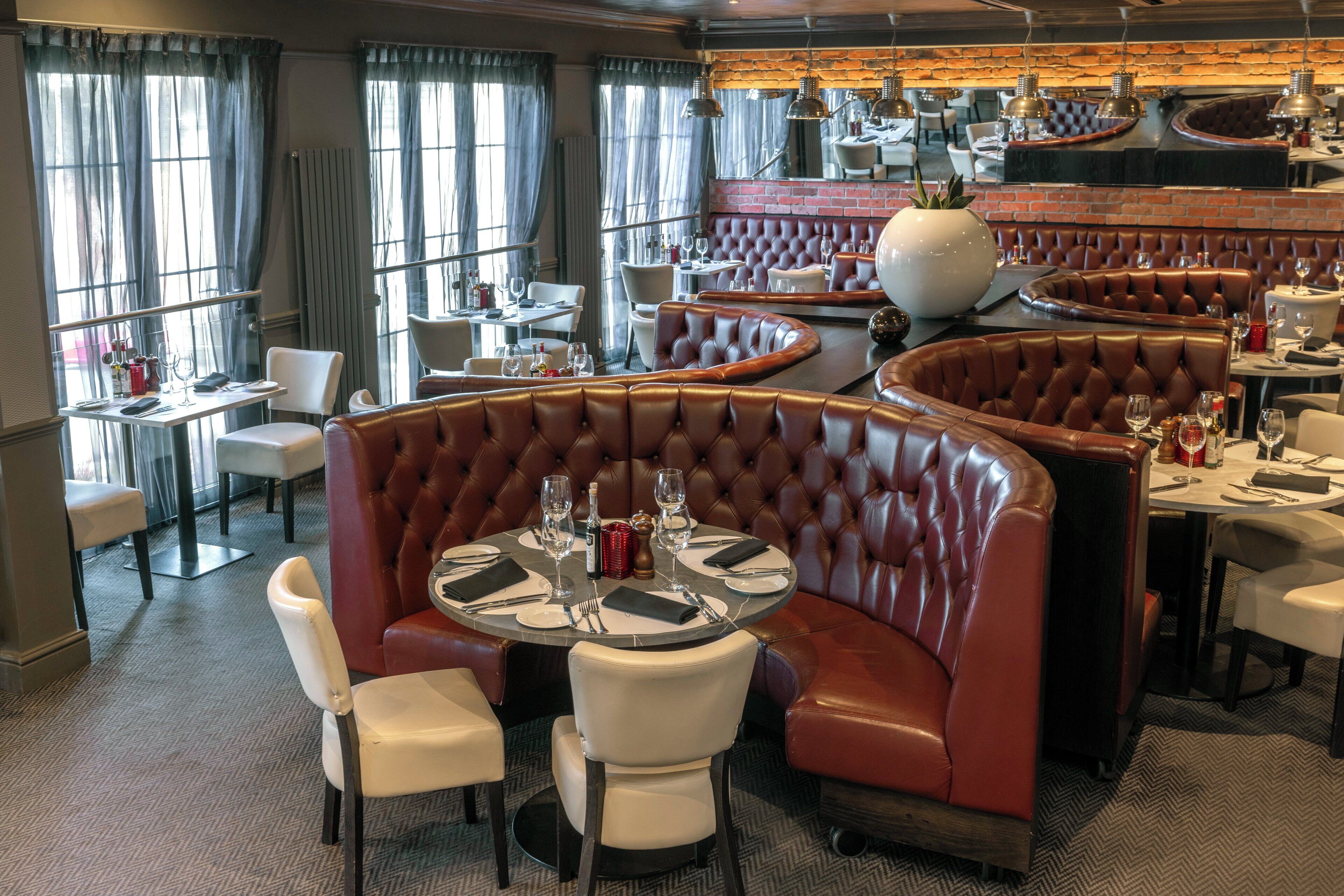 A restaurant with round tables and booths, featuring leather seating and a brick wall backdrop.