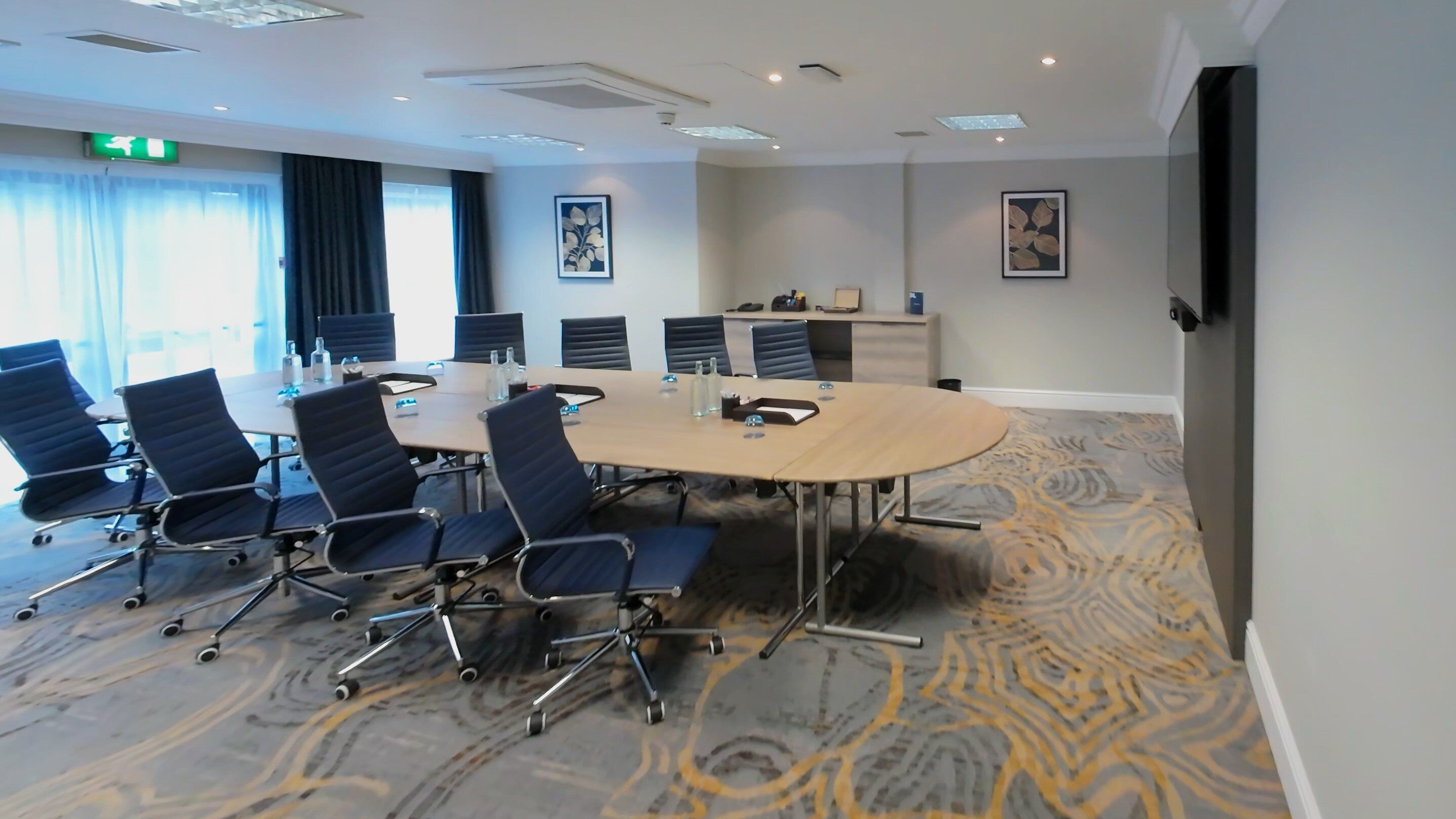 A conference room with a large oval table, black chairs, and a patterned carpet.
