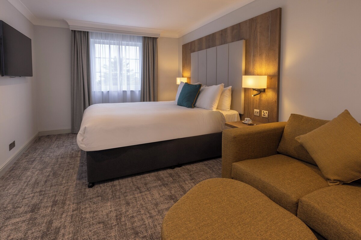 Une chambre d’hôtel avec un grand lit, un canapé, une télévision et une lampe fixée au mur.