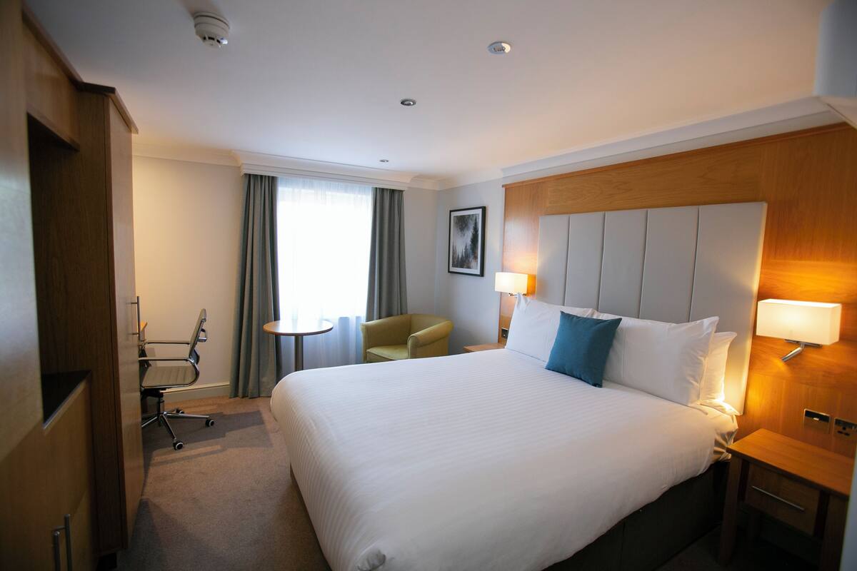 A hotel room with a large bed, a desk, a chair, a lamp, and a picture on the wall.