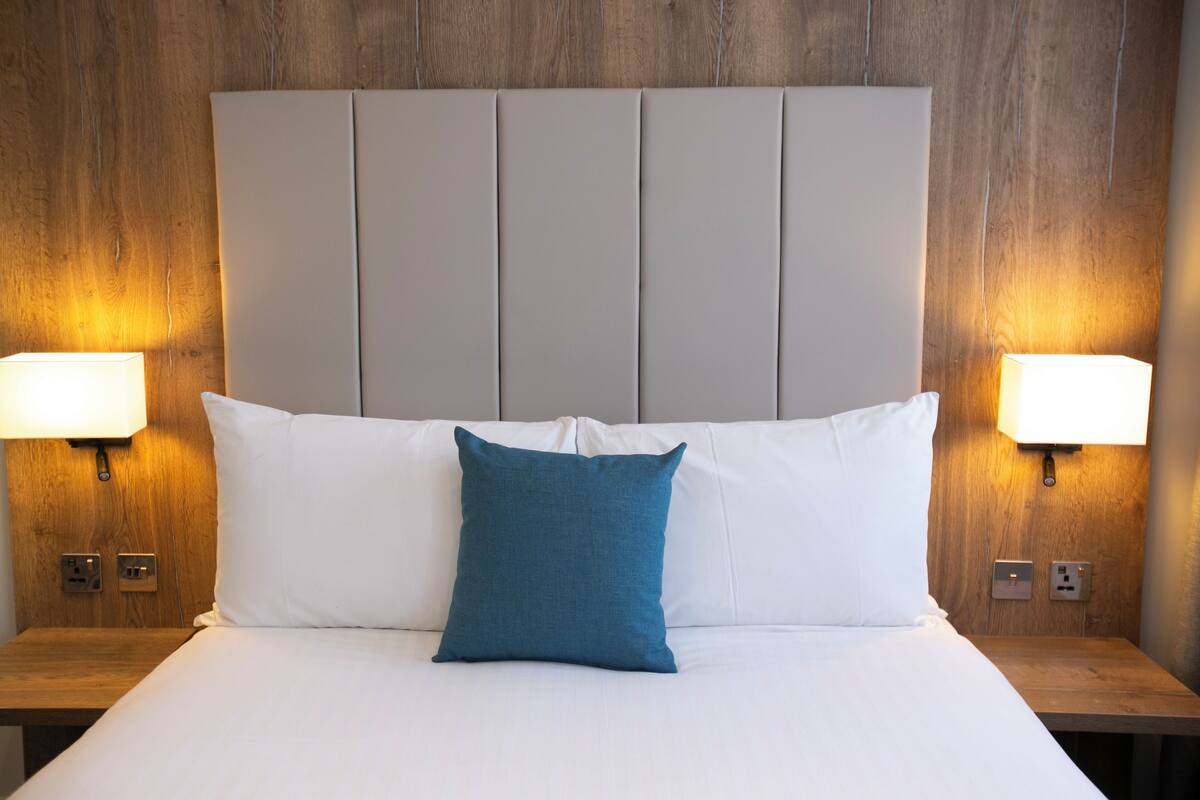 A neatly made bed with white linens and a single blue pillow, flanked by two bedside lamps on wooden nightstands.