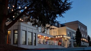 A modern hotel with a glass facade, a covered outdoor area, and a tree with string lights. - Crowne Plaza East Midlands Airport by IHG (Kegworth)