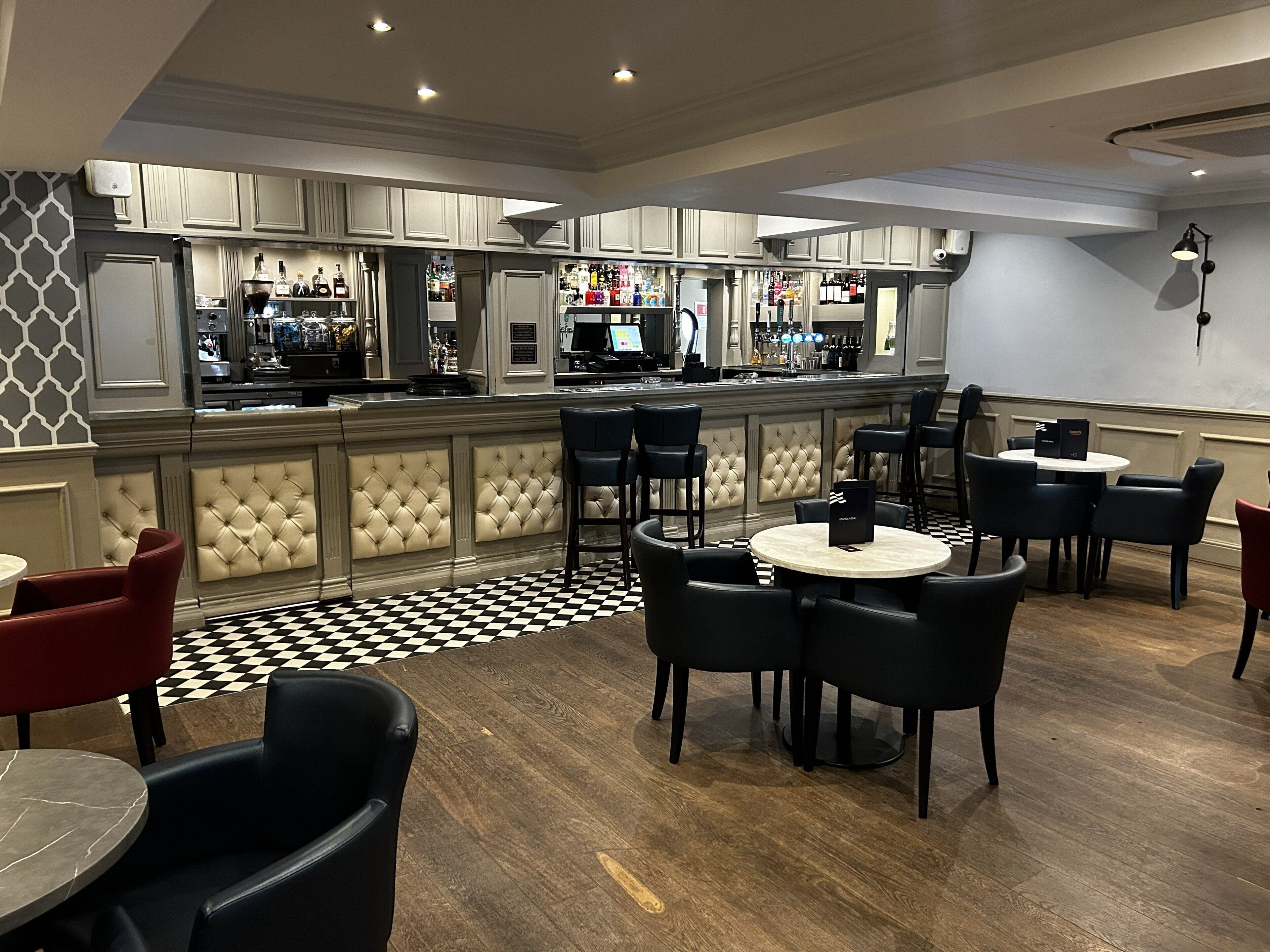 A bar area with a checkered floor, bar stools, and a bar counter with various bottles.