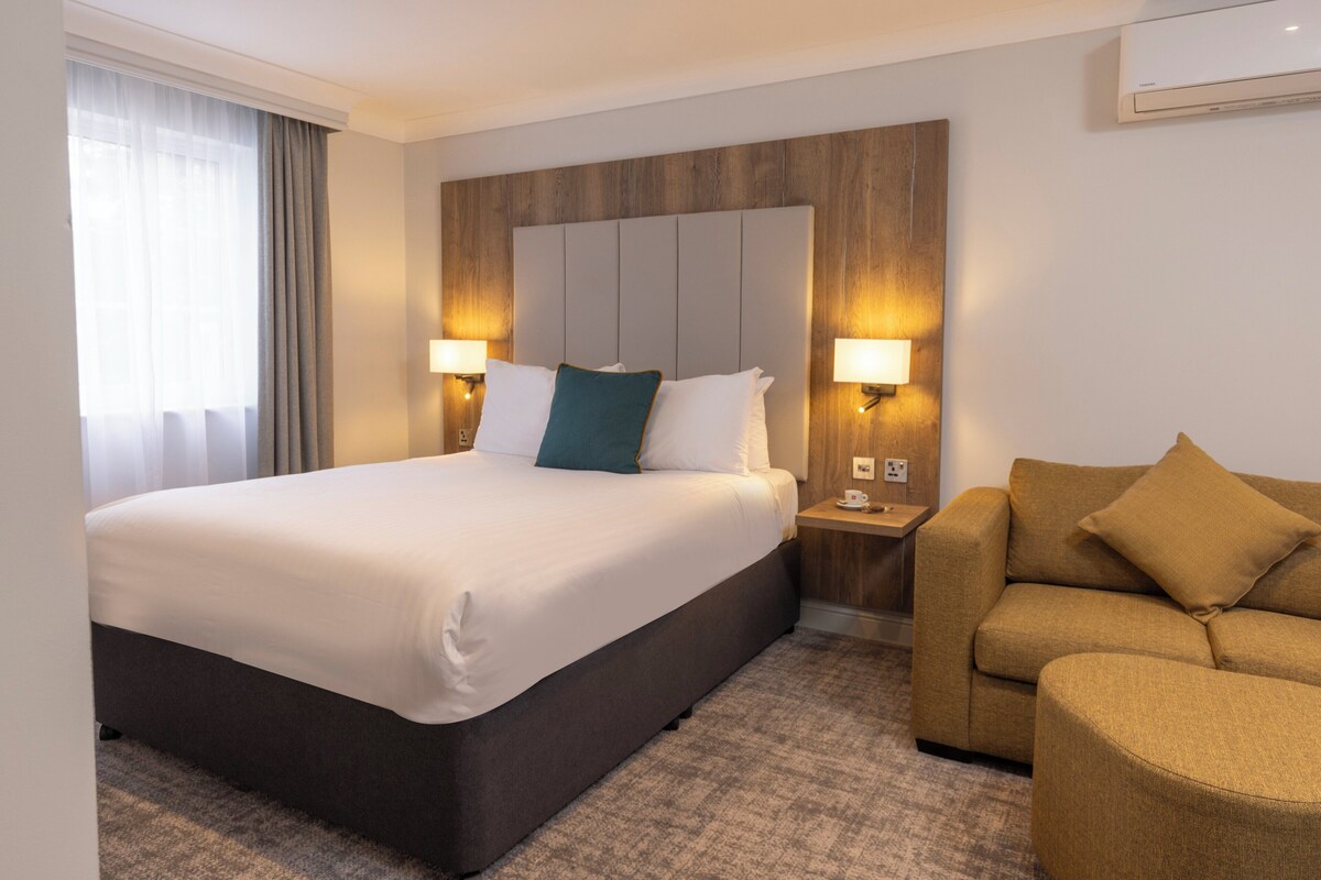 Une chambre d’hôtel avec un grand lit, un canapé, deux lampes de chevet et une tête de lit en bois.