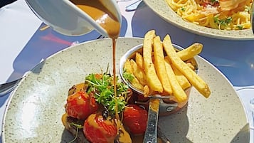 A meal with steak, fries, and sauce on a plate, with a wine glass and bottles in the background.