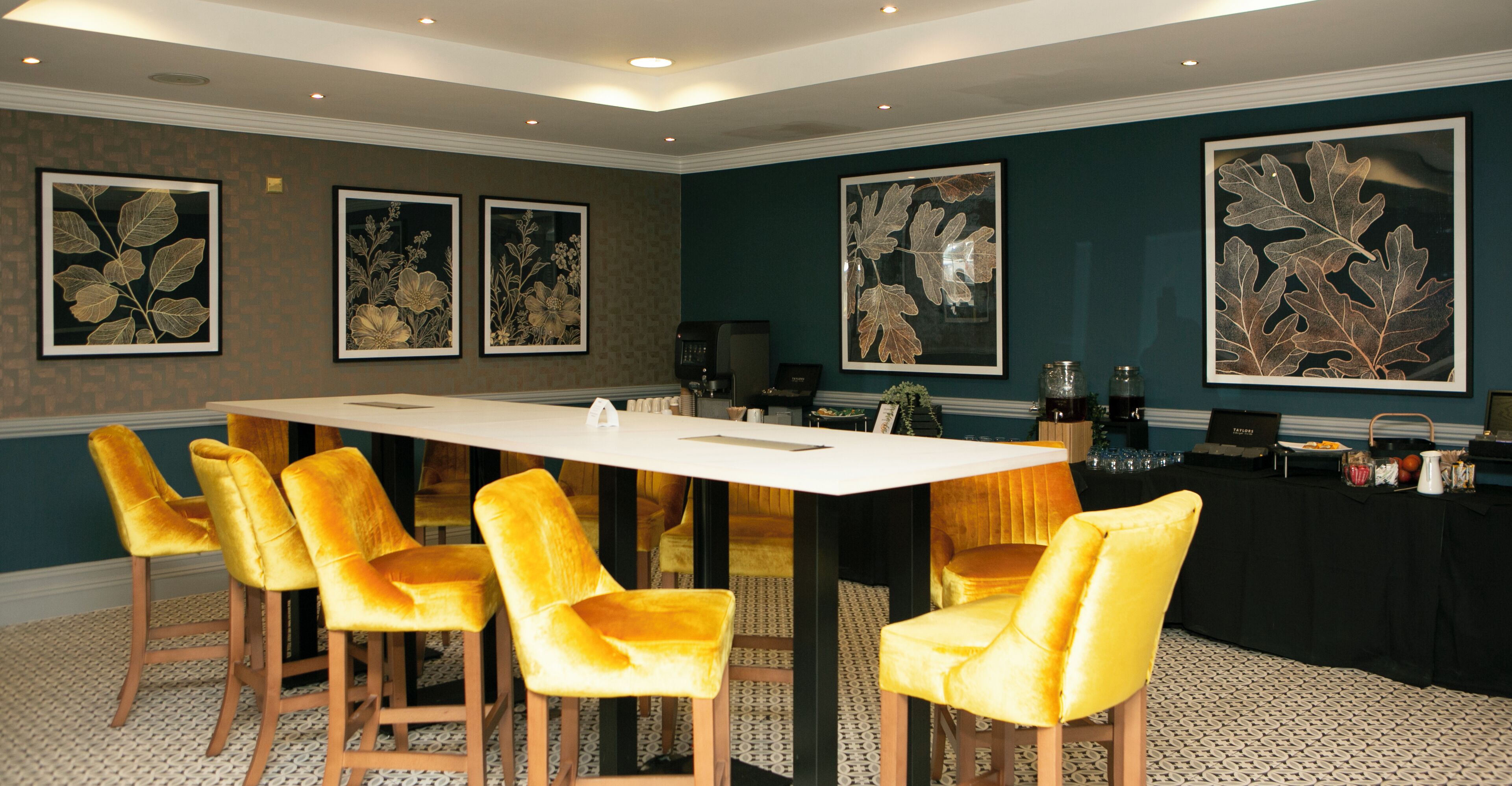 A conference room with a long table, six yellow chairs, and framed botanical artwork on the walls.