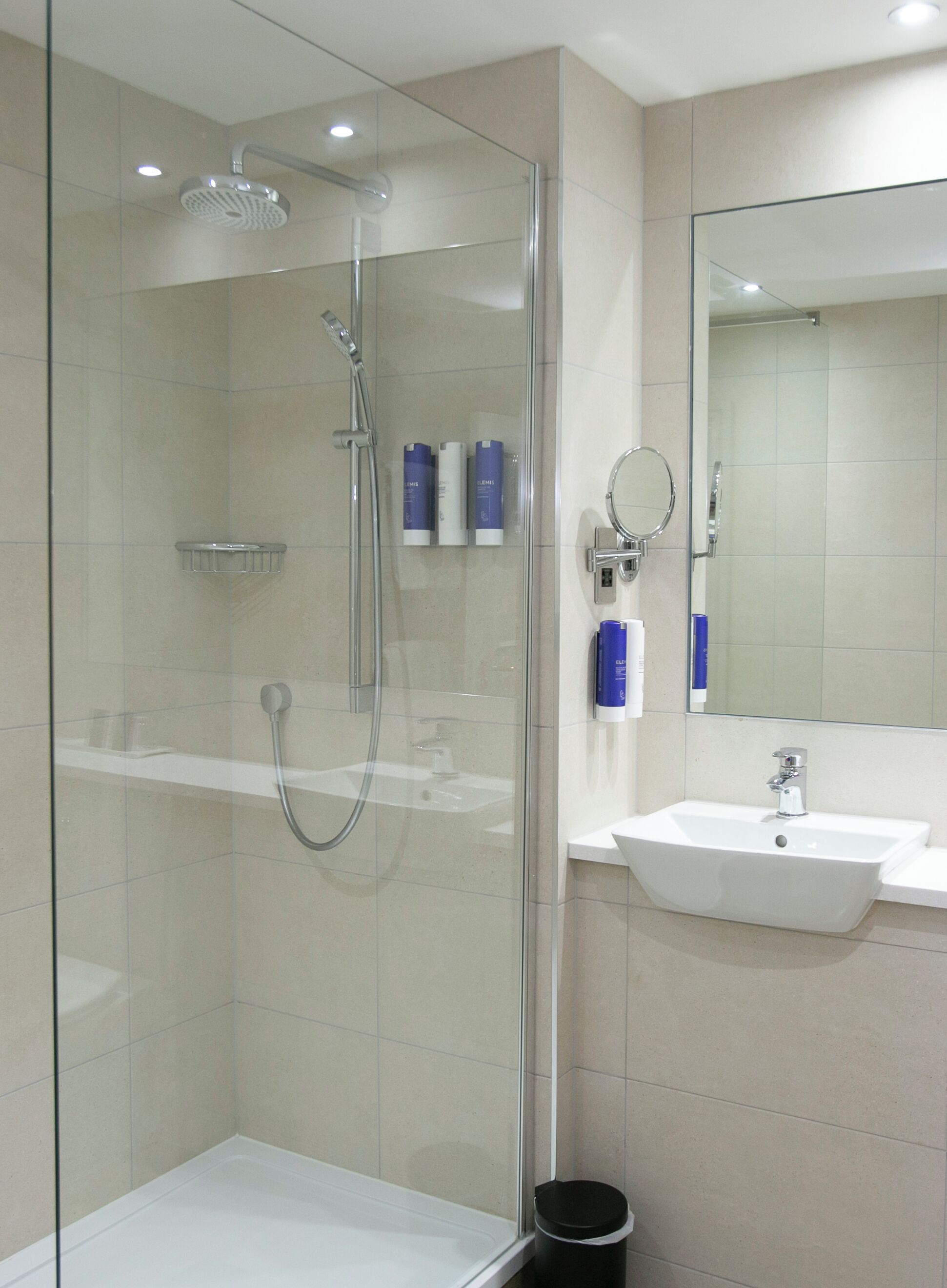 A modern bathroom with a glass-enclosed shower, a white sink, and a mirror above it.