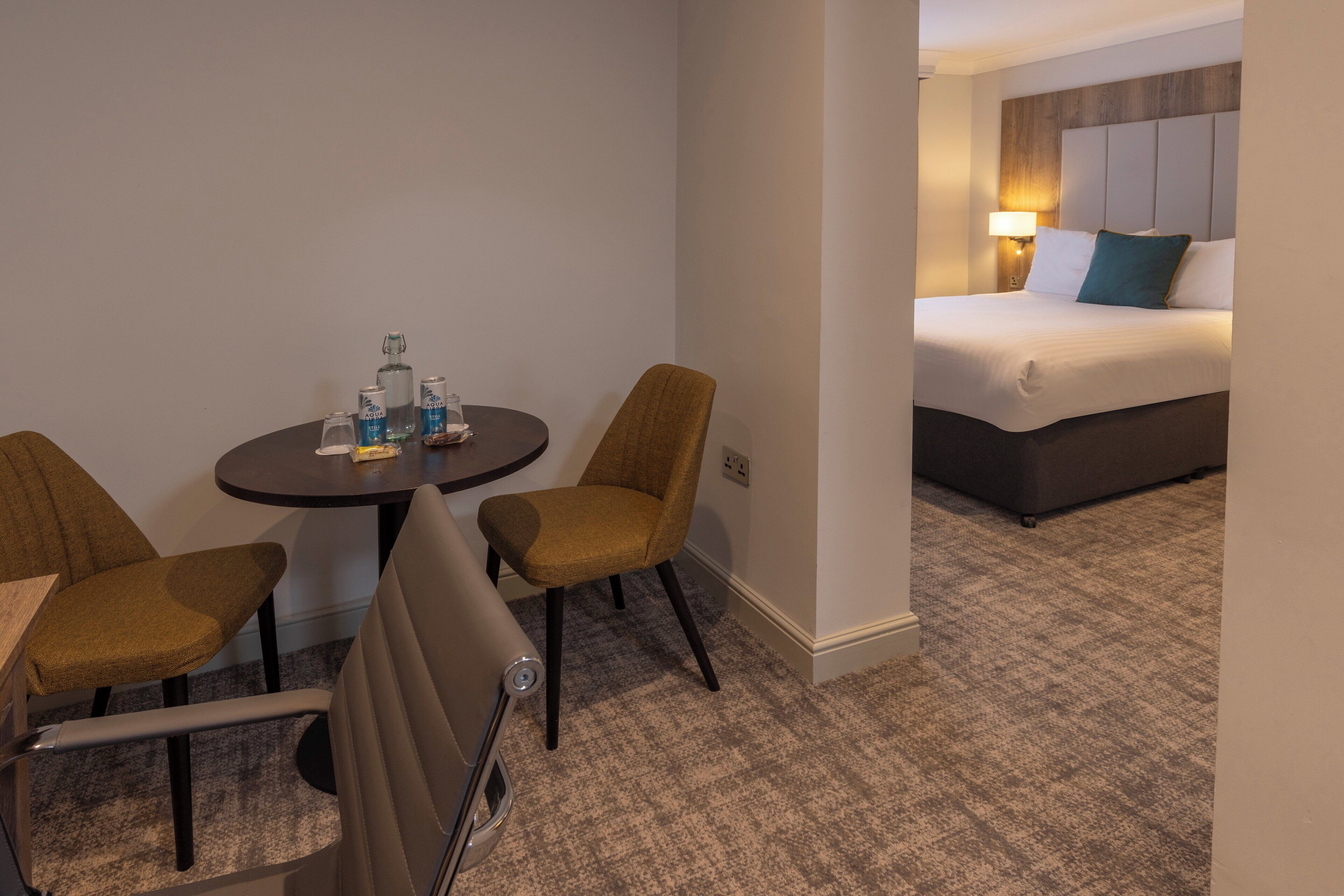 Una habitación de hotel con cama, una mesita con sillas y un minibar.