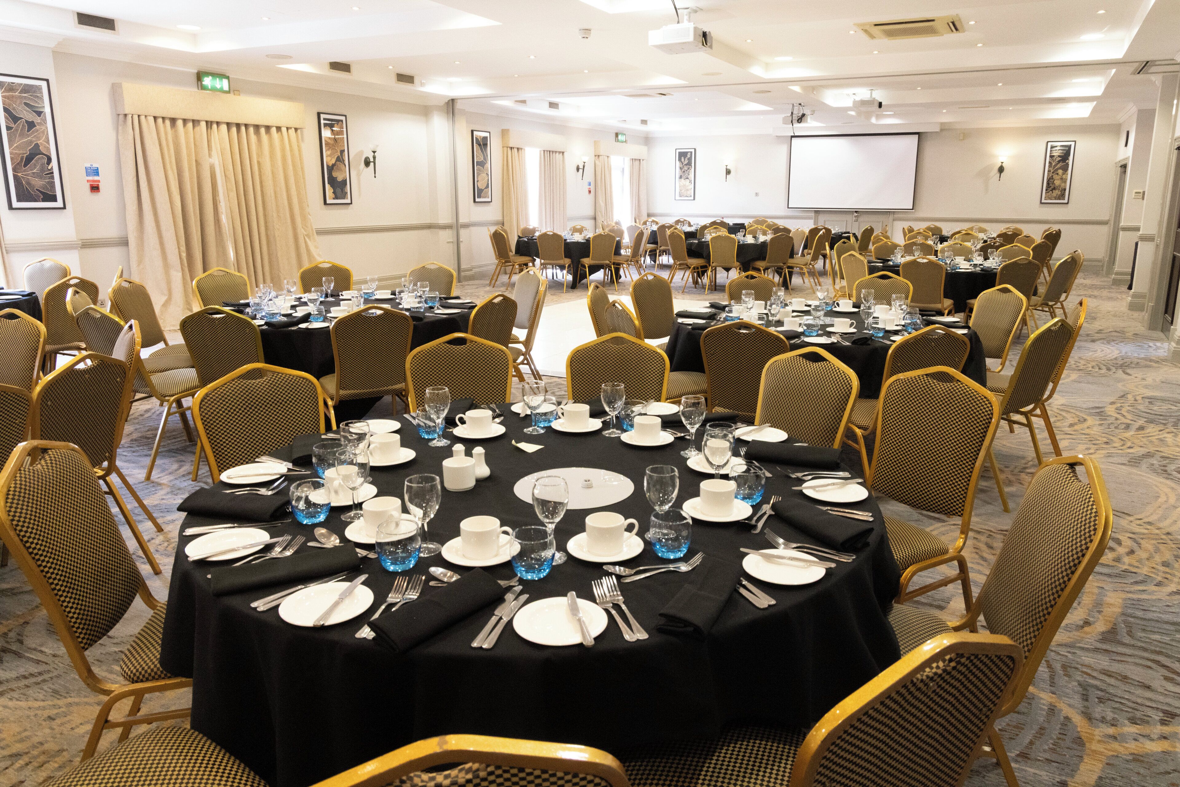 A conference room with round tables, chairs, and a projector screen.