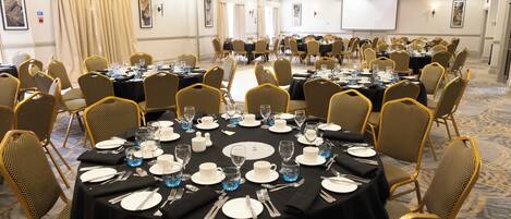 A conference room with round tables, chairs, and a projector screen.
