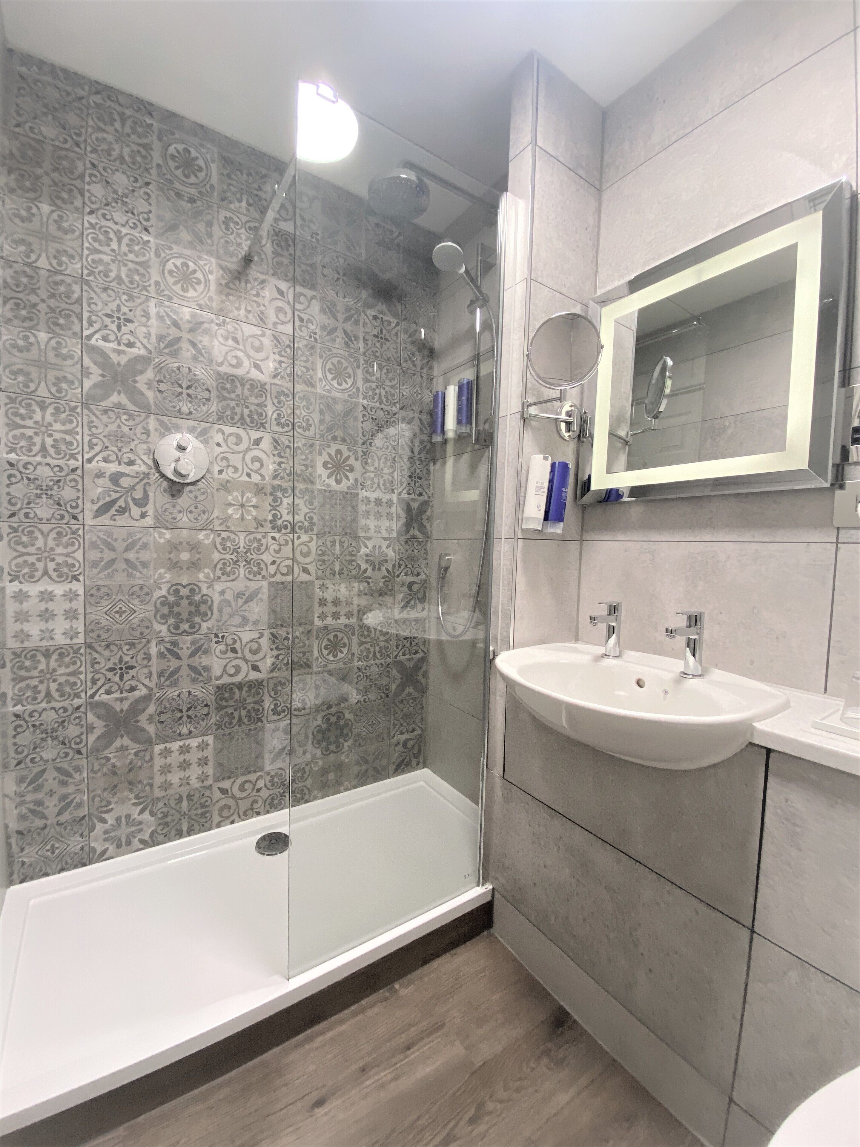 A modern bathroom with a glass-enclosed shower, a white bathtub, and a vanity with a mirror.