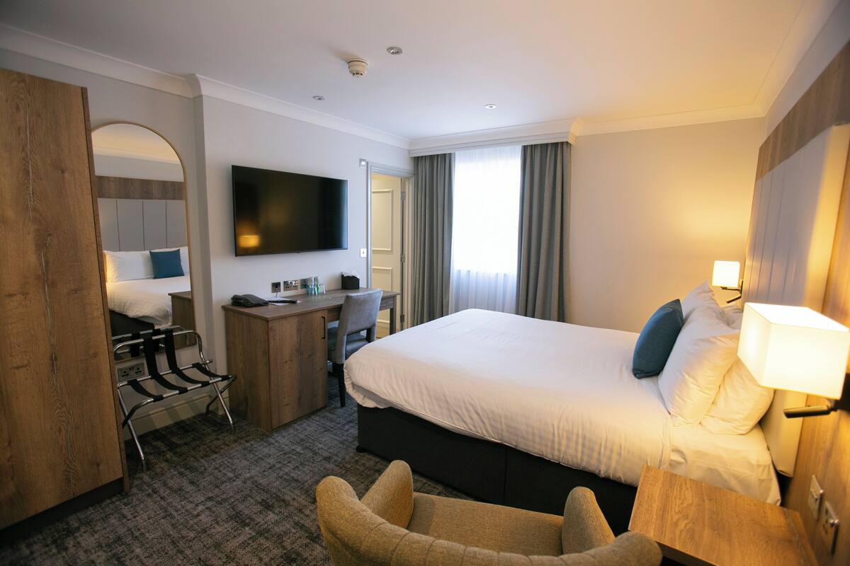 A hotel room with a large bed, a desk with a chair, a television, and a wardrobe.