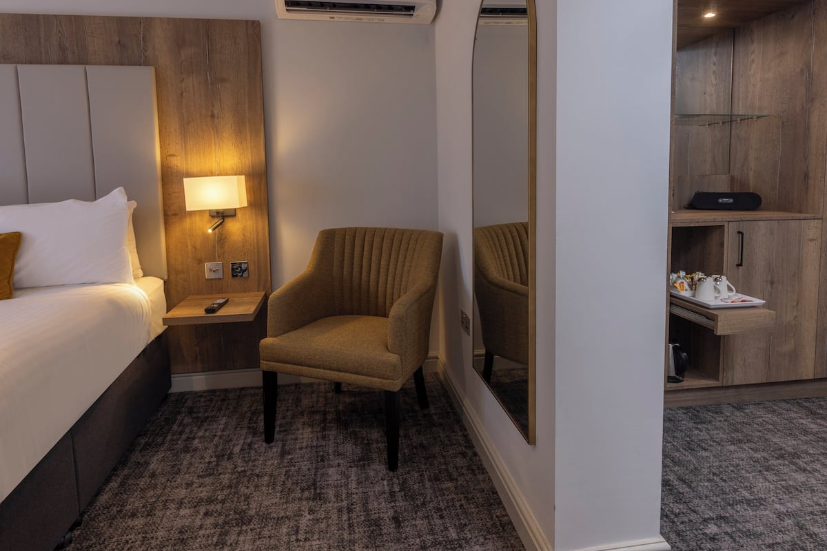 A hotel room with a bed, a nightstand, a lamp, a chair, a mirror, and a wardrobe.