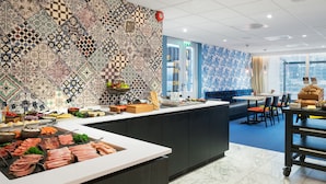 A modern restaurant with a tiled backsplash, a buffet counter with various food items, and a seating area with a blue sofa and chairs. - Thon Hotel Tønsberg Brygge (Tønsberg)