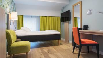 A hotel room with a bed, a desk, a chair, a TV, and a lamp.