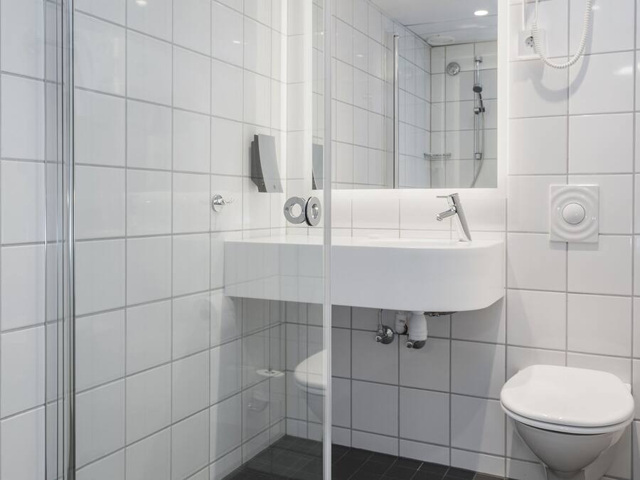 Een moderne badkamer met een douchecabine van glas, een witte wastafel en een toilet.
