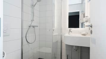 Un baño moderno con ducha envuelta en vidrio, un lavamanos blanco y un espejo sobre él.