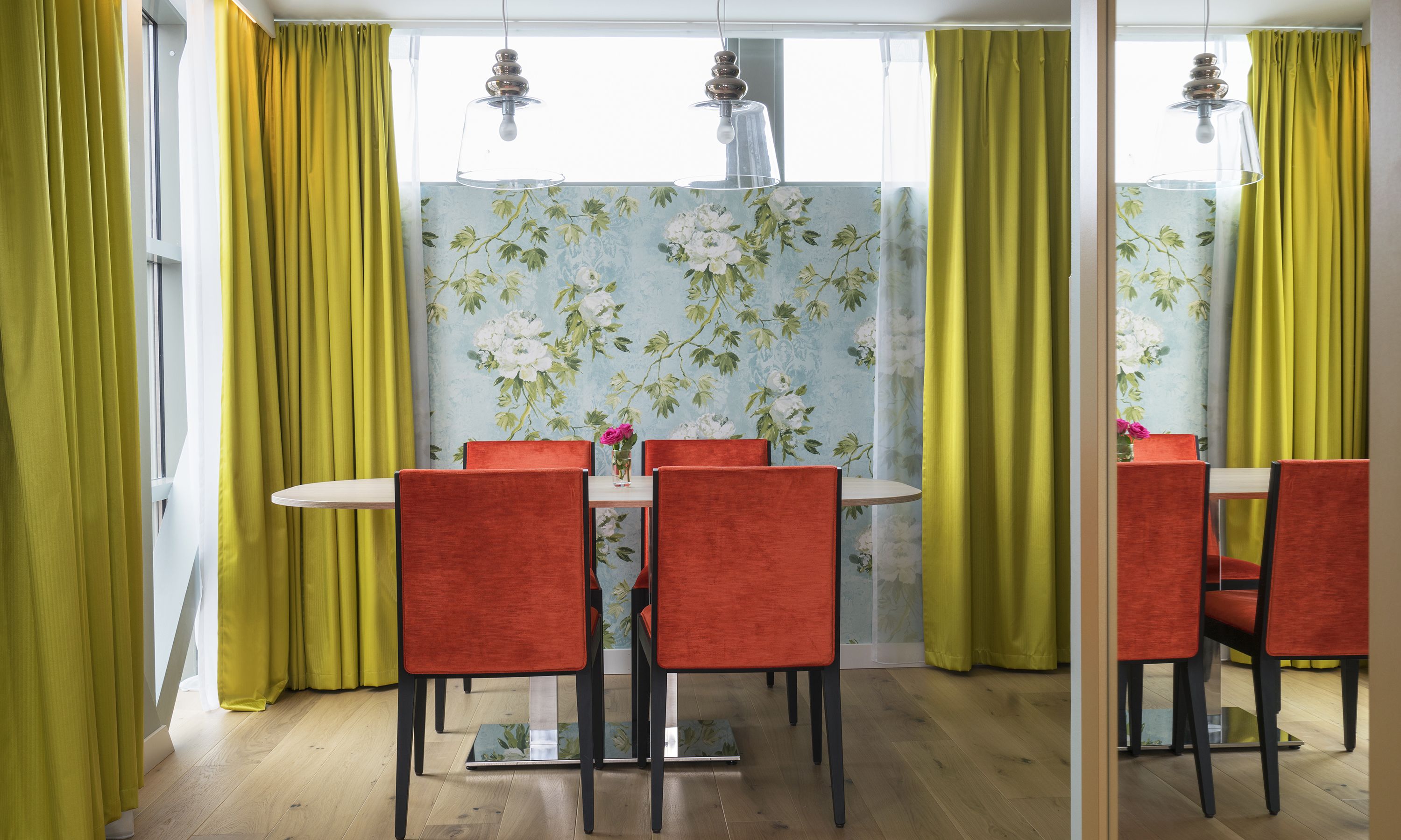 A dining area with a round table, red chairs, and yellow curtains.
