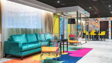 Una habitación de hotel moderna con un sofá color turquesa, una mesa de vidrio y una alfombra colorida.