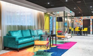 Een moderne hotelkamer met een blauwgroene bank, een glazen tafel en een kleurrijk vloerkleed.