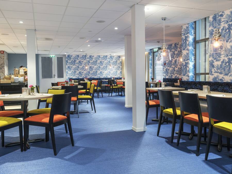 Un restaurante con papel tapiz azul estampado, varias mesas con sillas y un suelo cubierto de moqueta azul.