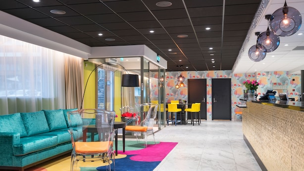 A modern hotel lobby with a teal sofa, clear chairs, a reception desk, and a colorful rug. - Thon Hotel Tønsberg Brygge (Tønsberg)