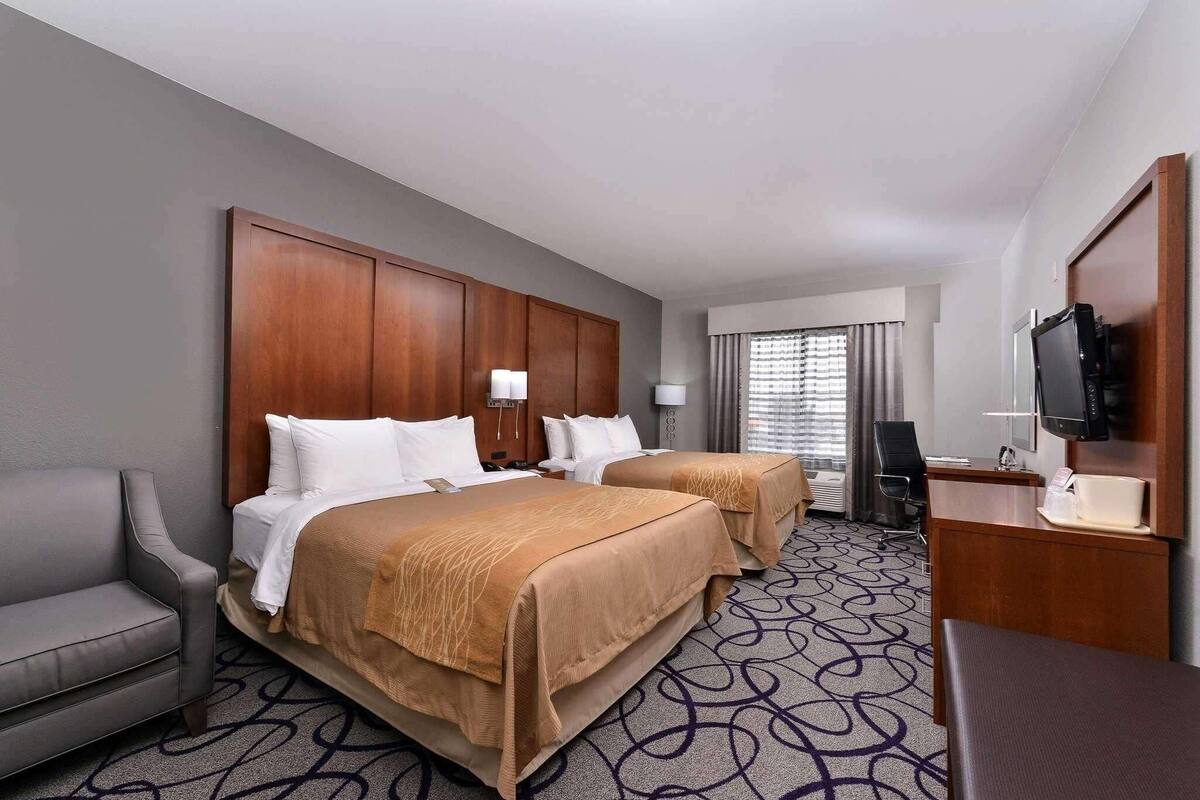 A hotel room with two beds, a desk, a TV, and a chair.