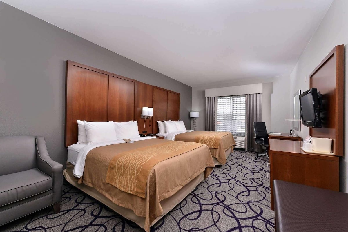 A hotel room with two beds, a desk, a TV, and a chair.