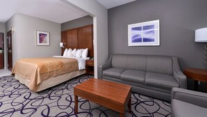 A hotel room with a bed, a grey sofa, a wooden coffee table, and a patterned carpet. - Comfort Inn & Suites Frisco - Plano (Frisco)