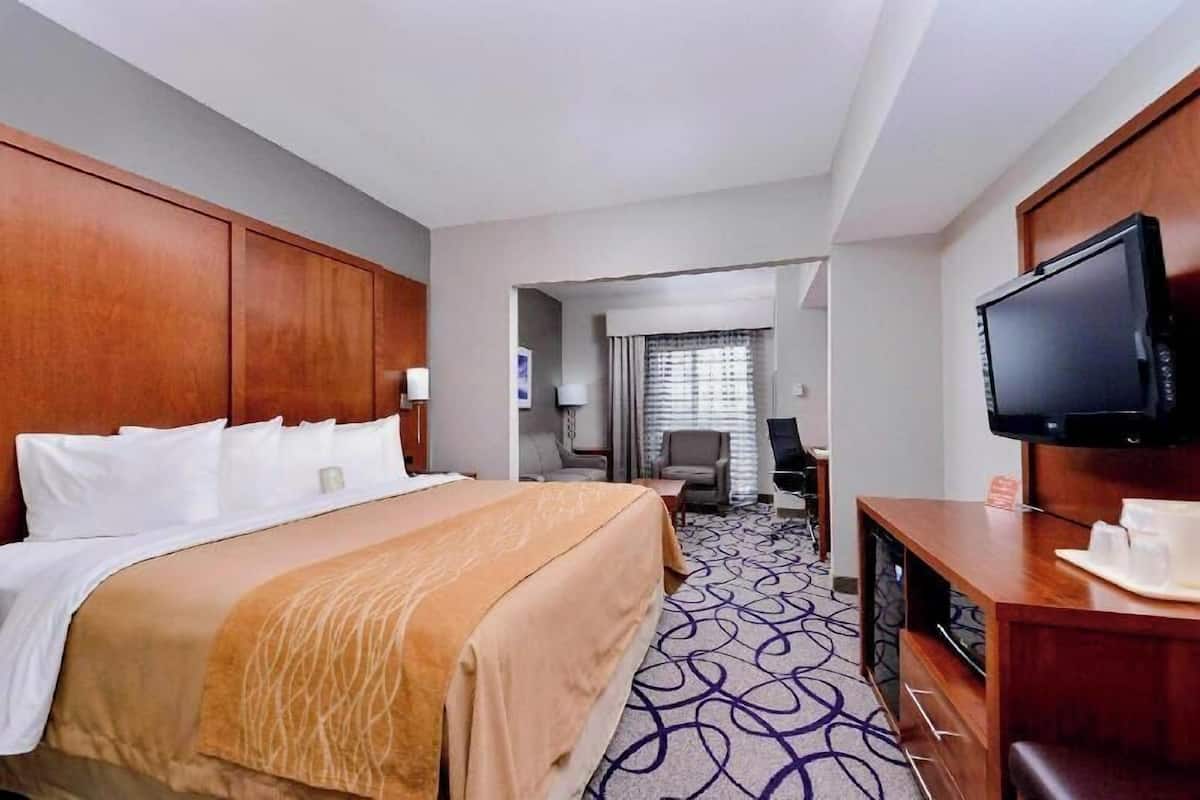 A hotel room with a large bed, a desk with a flat-screen TV, a coffee maker, and a view of the hallway.