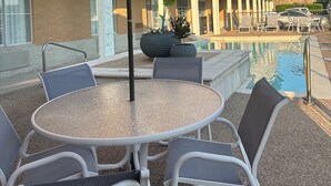 A poolside area with a round table and chairs, a red umbrella, and a building in the background. - Comfort Inn & Suites Frisco - Plano (Frisco)
