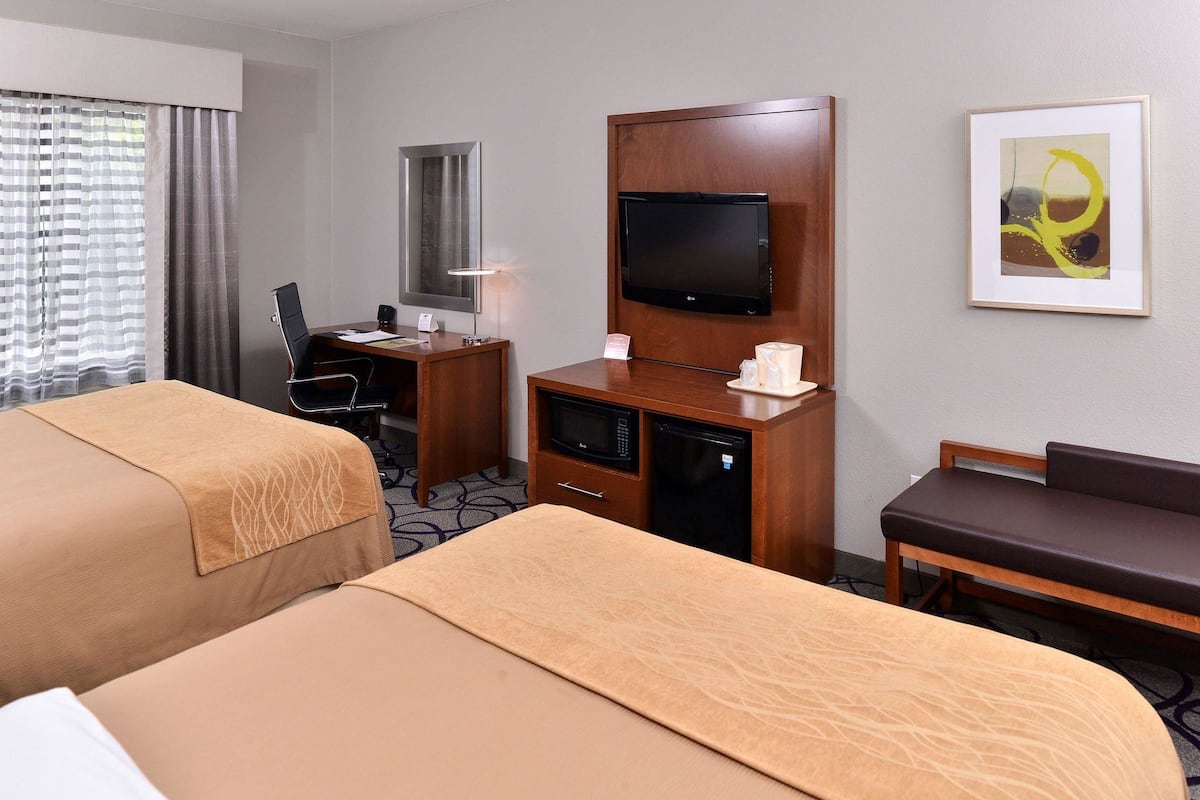 A hotel room with two beds, a desk with a computer, a TV, a microwave, and a small seating area.