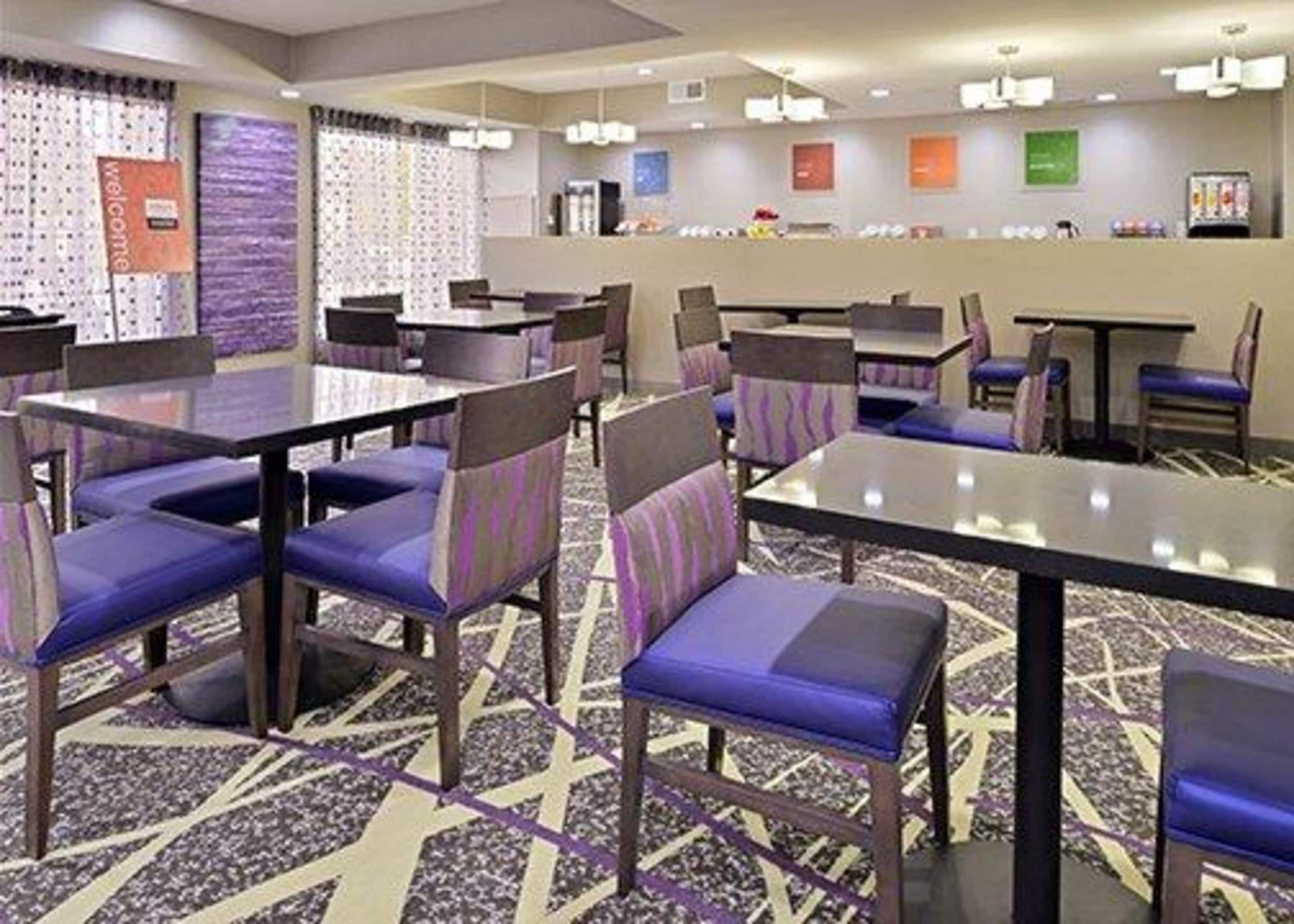 Un vestíbul d'hotel amb diverses taules i cadires, una recepció i una catifes amb dibuixos.