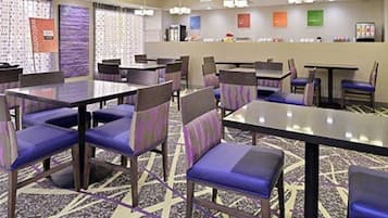 Un vestíbul d'hotel amb diverses taules i cadires, una recepció i una catifes amb dibuixos.