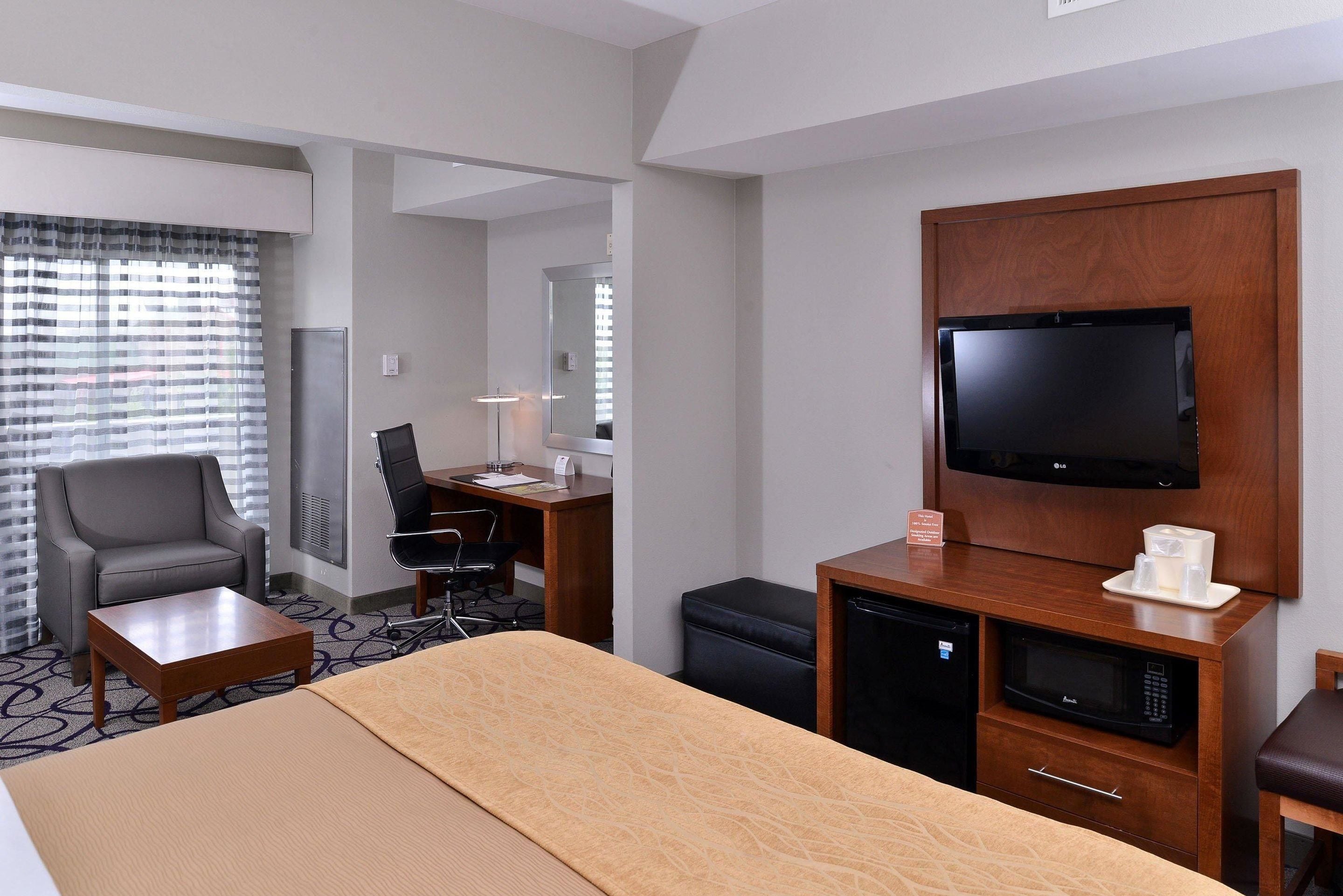 A hotel room with a bed, a desk, a chair, a television, a coffee maker, and a microwave.